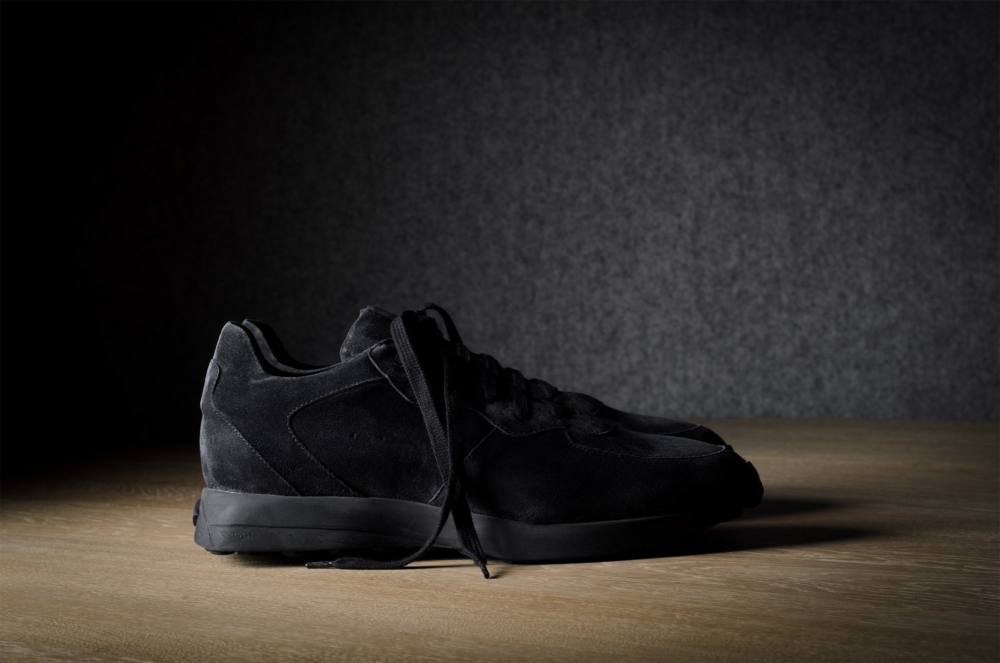 Black suede sneakers on a grey and brown wood background.