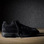 Black suede sneakers on a grey and brown wood background.