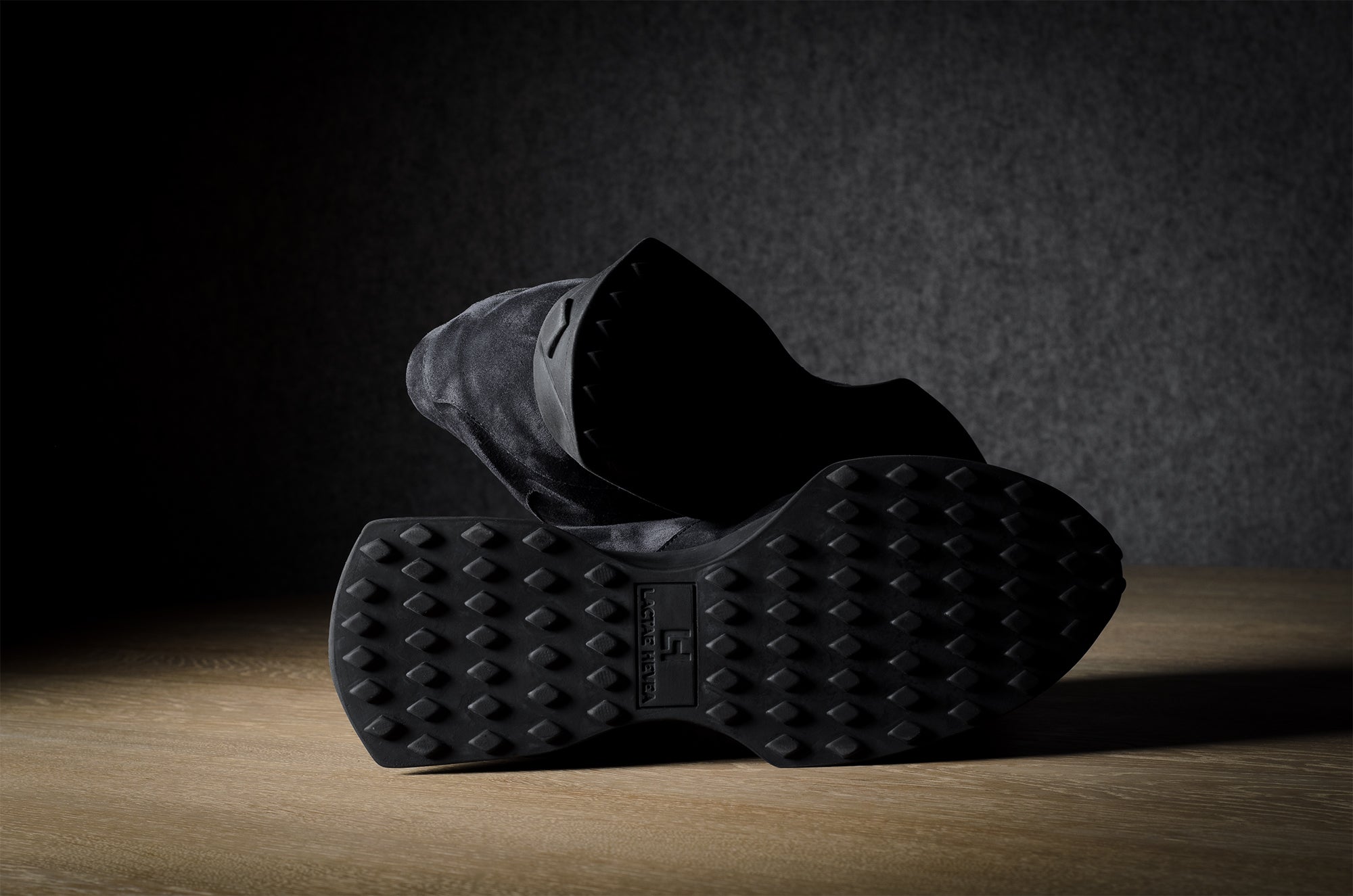 Black suede sneakers on a grey and brown wood background.
