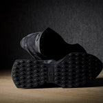 Black suede sneakers on a grey and brown wood background.