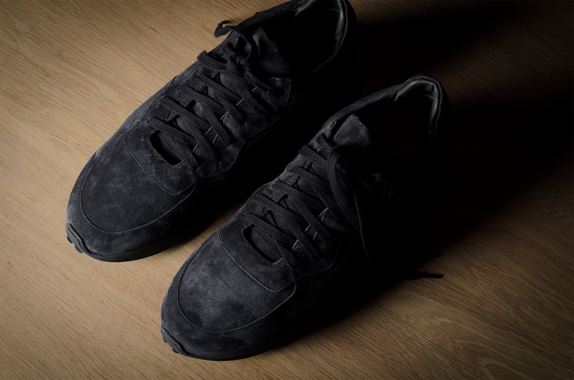 Black suede sneakers on a brown wood background.