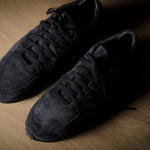 Black suede sneakers on a brown wood background.