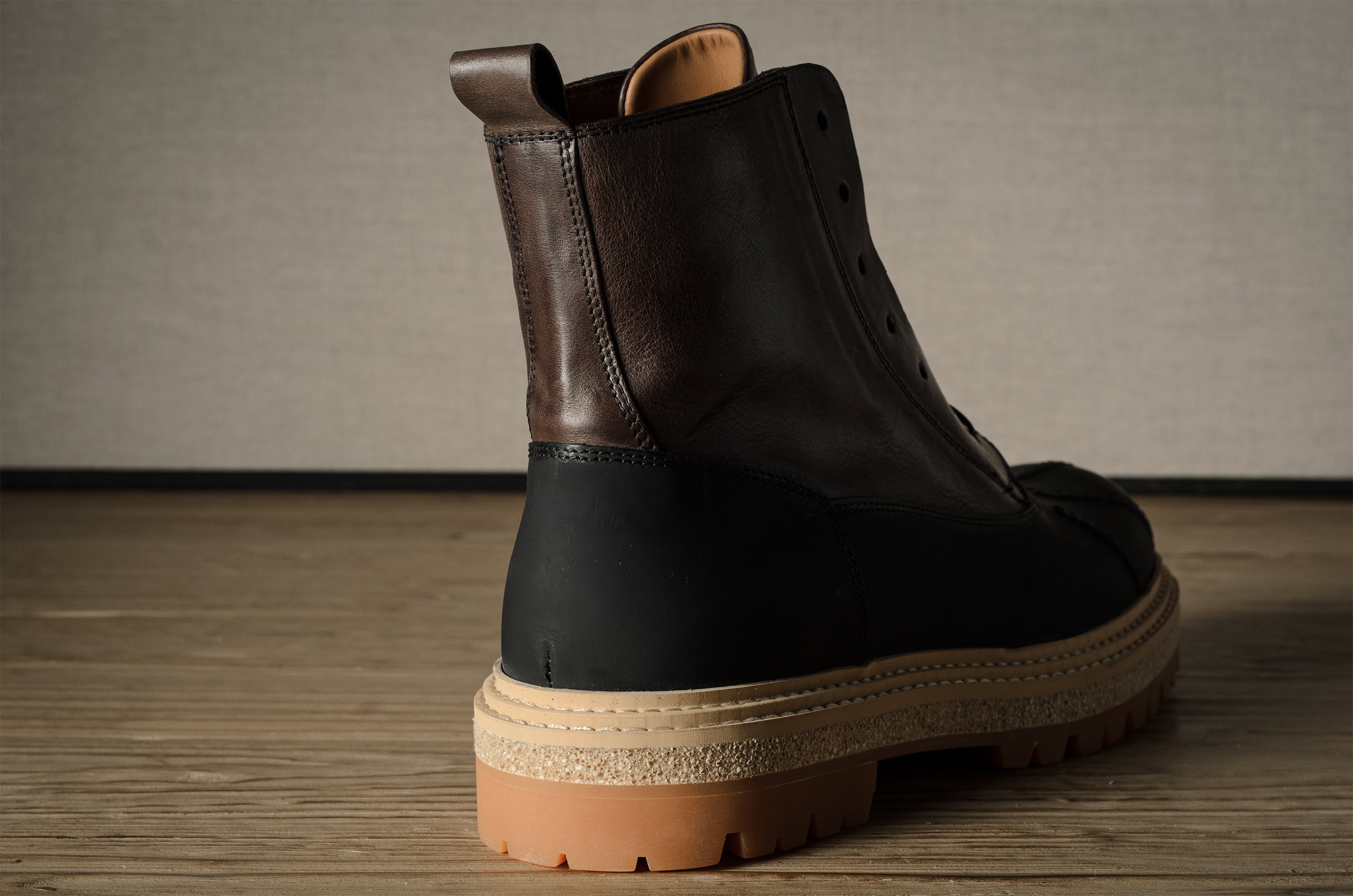 Brown leather hiking boot with a black sole on a wooden floor