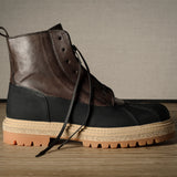 Brown and black leather hiking boot with a thick sole on a wooden floor.
