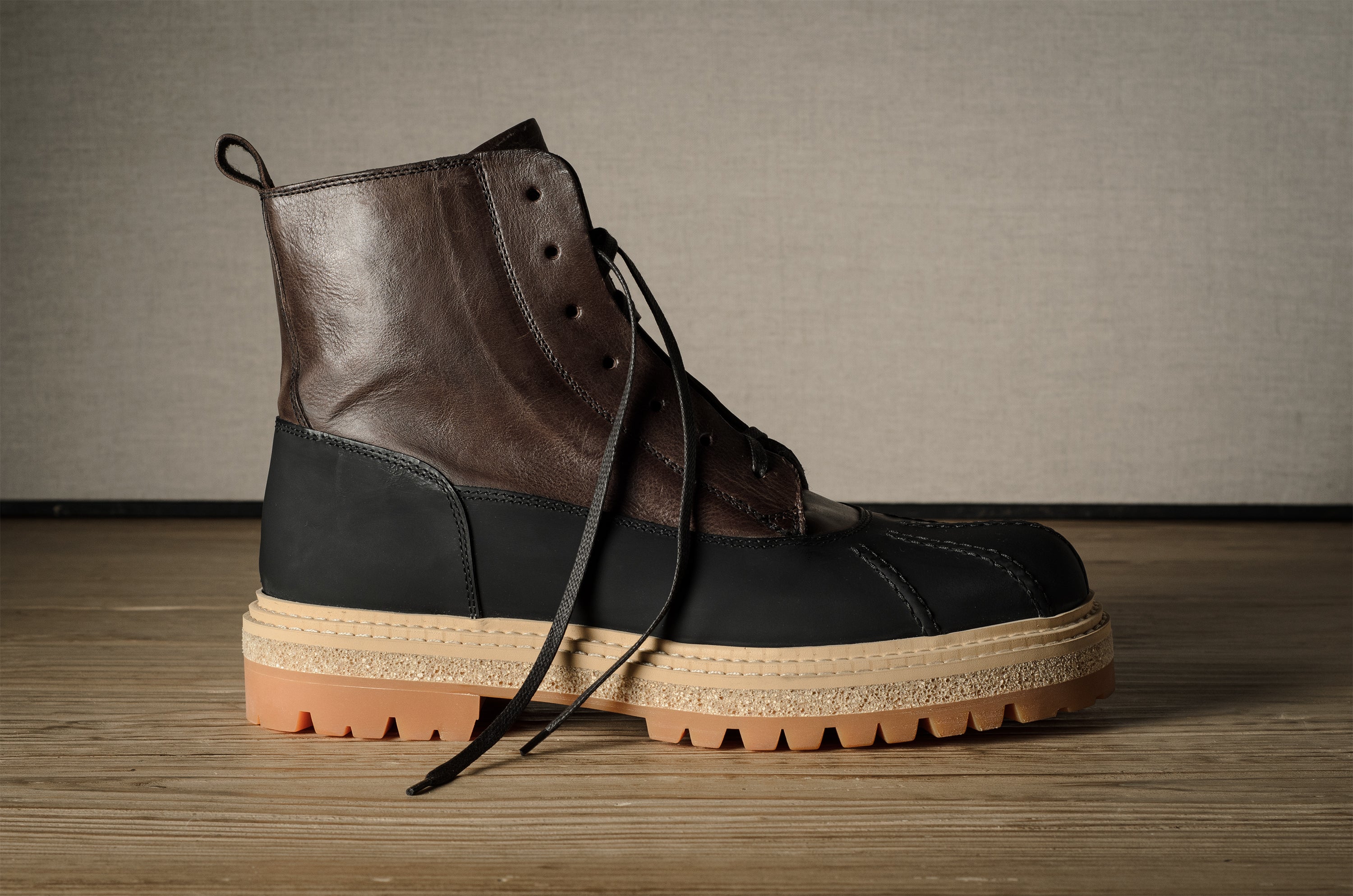 Brown and black leather hiking boot with a thick sole on a wooden floor.