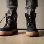 Brown leather hiking boots with tan soles worn by a person on a wooden floor.