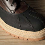 Black leather hiking boot with a brown sole on a wooden surface