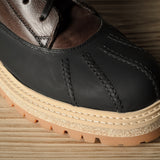 Black leather hiking boot with a brown sole on a wooden surface