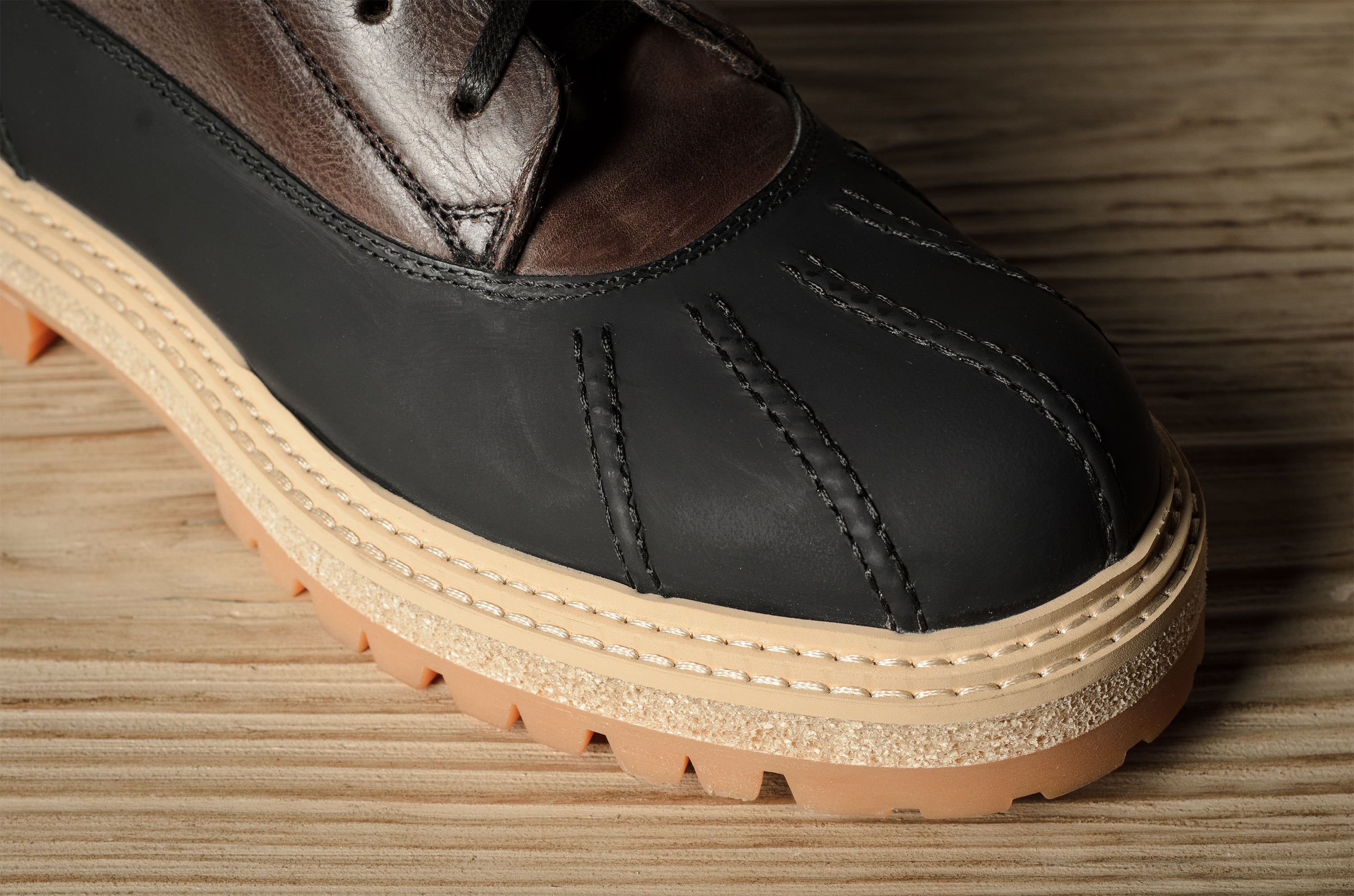 Black leather hiking boot with a brown sole on a wooden surface
