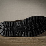 Close-up of a black boot sole on a wooden floor with a neutral wall background