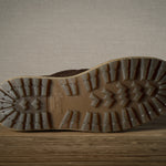 Close-up of a brown boot sole with tread pattern on a wooden floor.