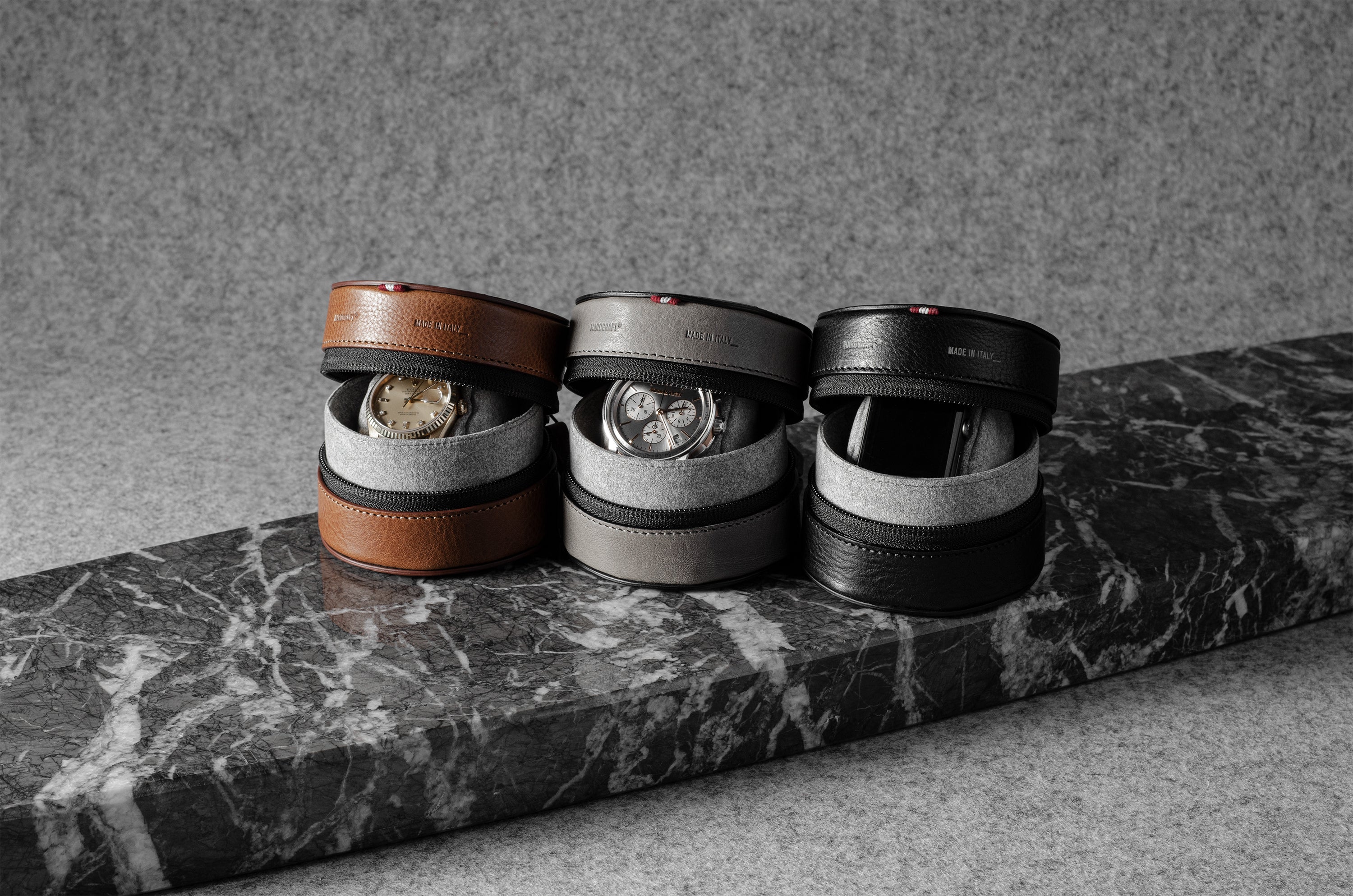 Three watch cases on a marble surface with a neutral background