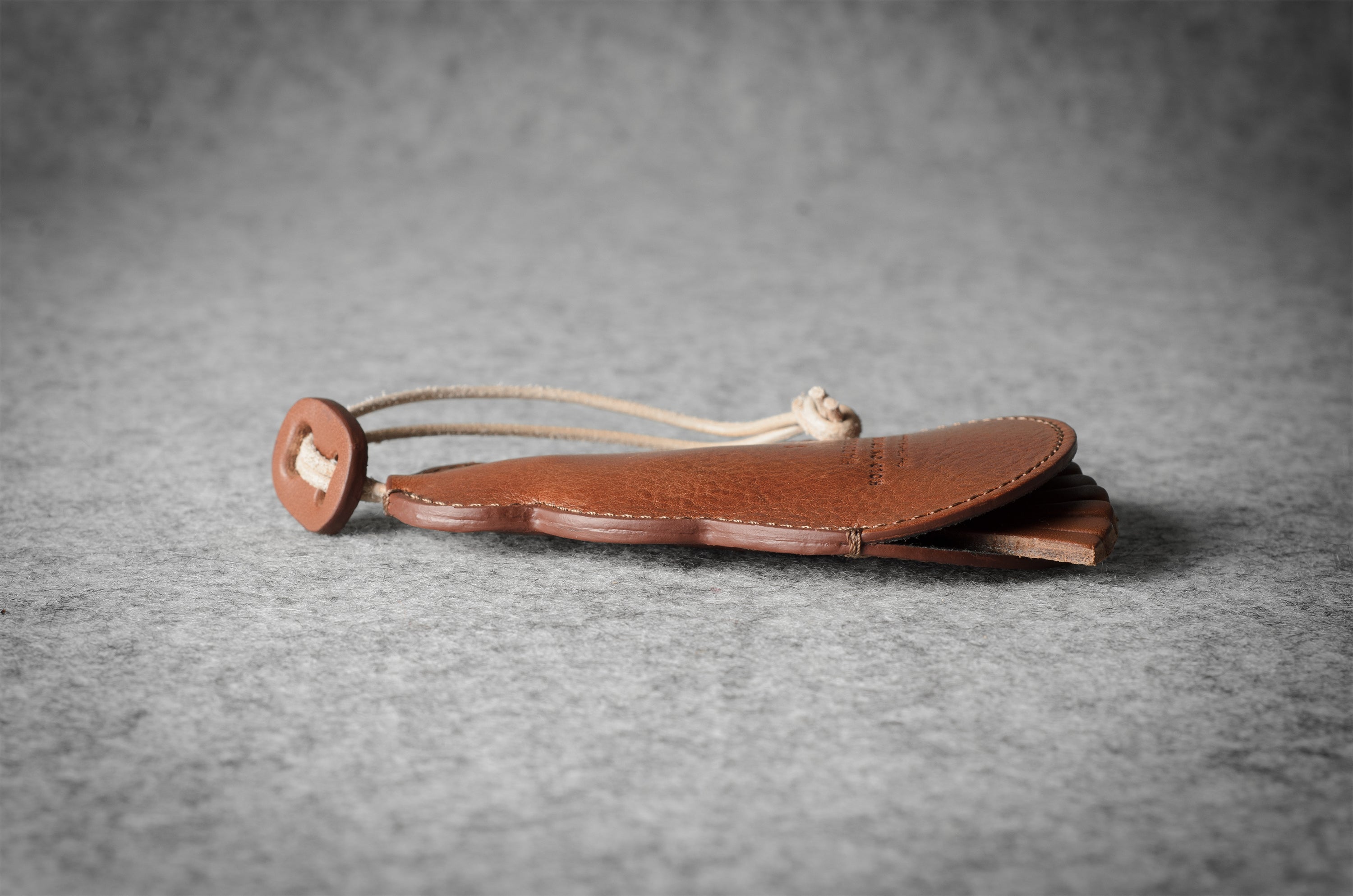 Brown leather keypouch with a leather string on a gray background