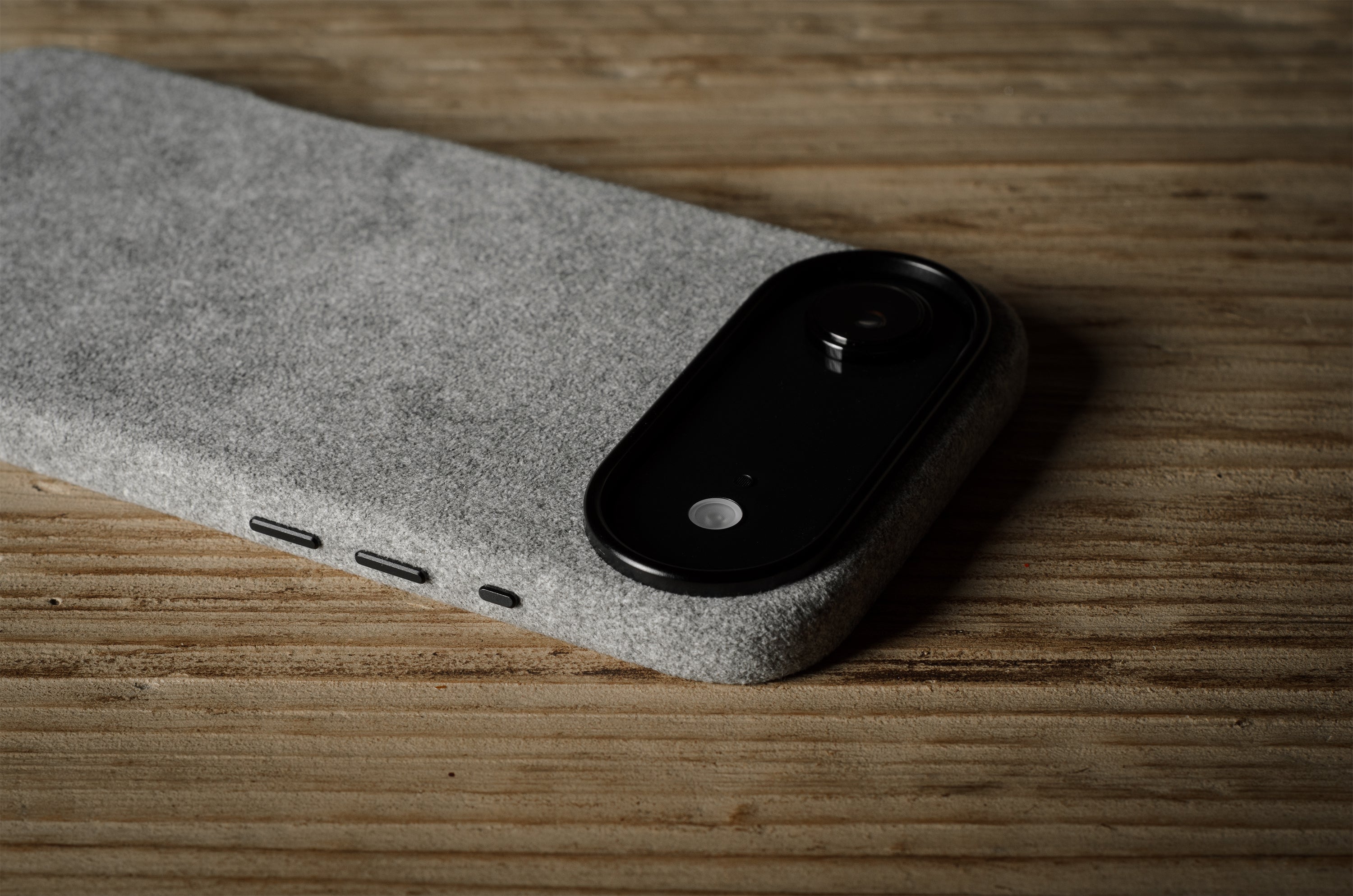 Black iPhone in grey case on a textured gray surface with a wooden background