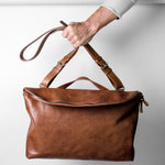 Brown leather handbag held by a hand against a light gray background