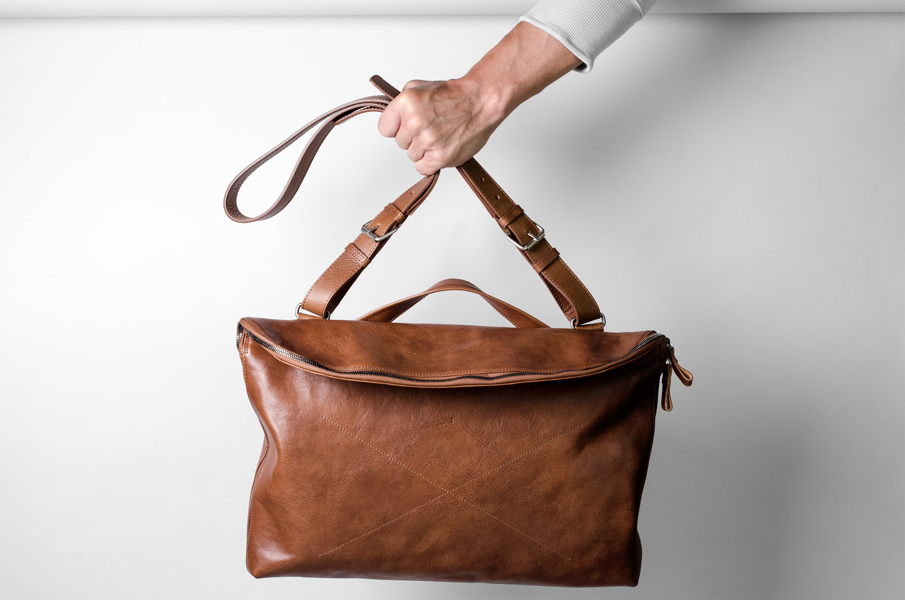 Brown leather handbag held by a hand against a light gray background