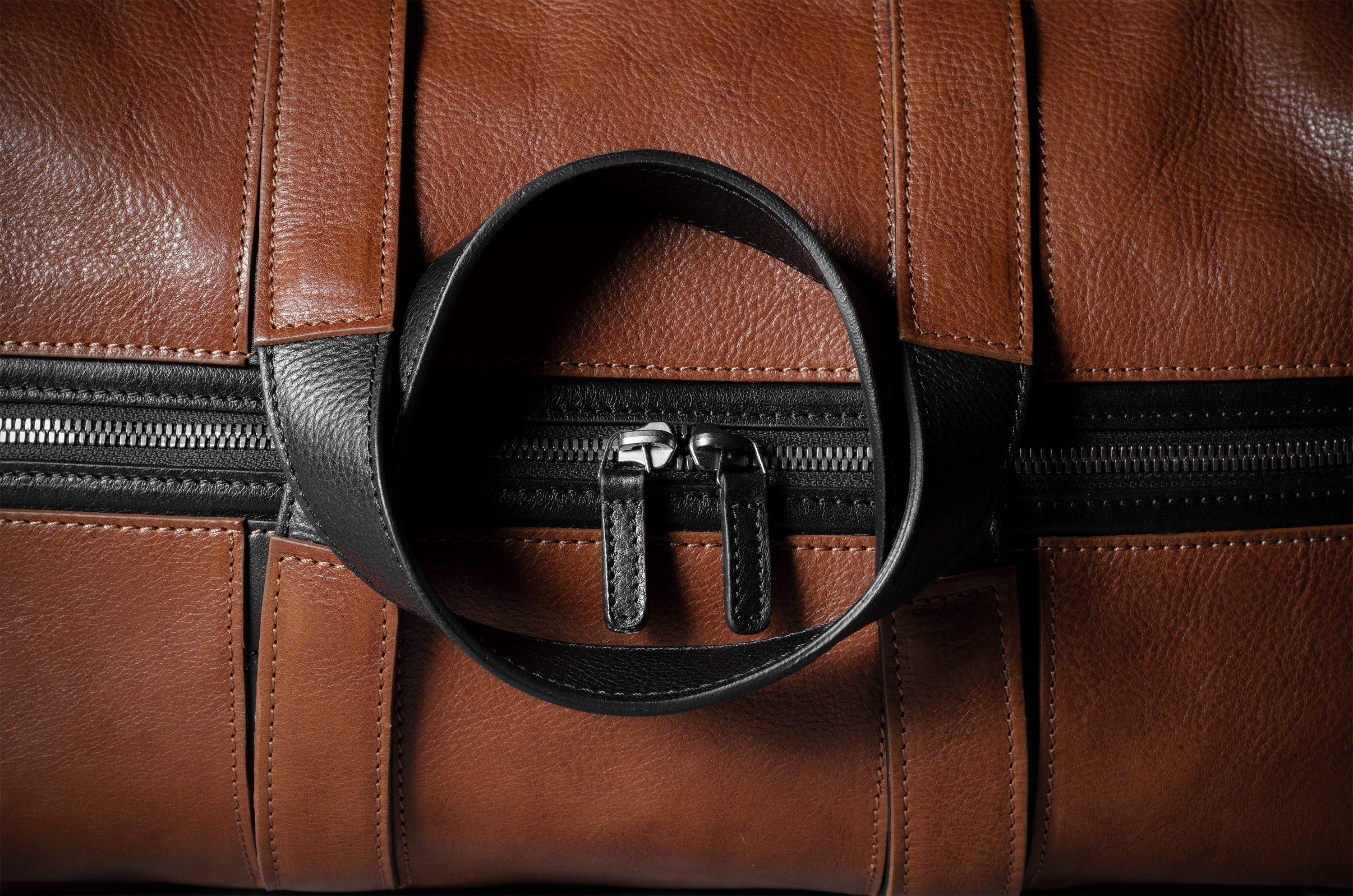 Close-up of a brown leather bag with black zipper and handle.