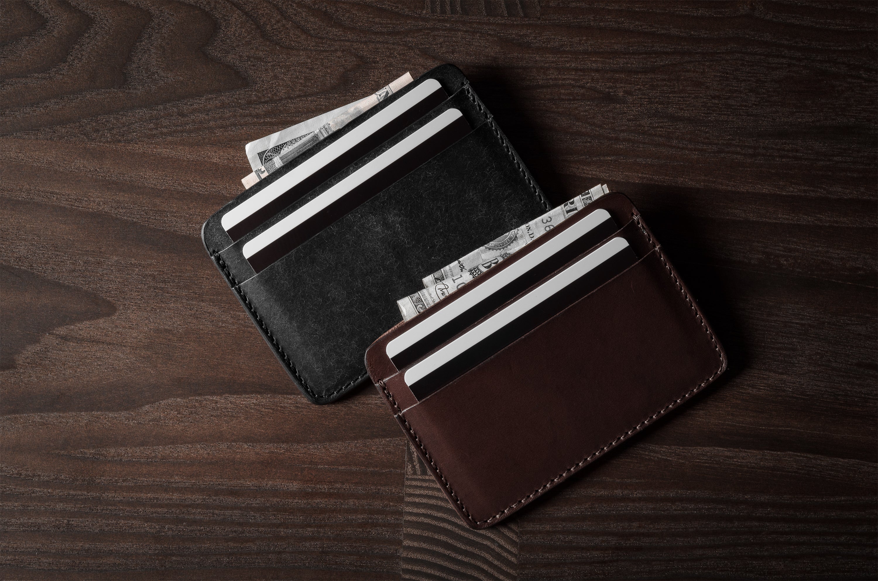 Two card cases on a dark wood background, one in brown, one in black with cards inside.