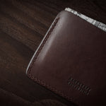 Brown leather card case with cash inside on a dark wood background.