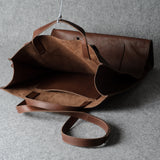 A brown leather tote bag with a matching shoulder strap, shown open against a textured gray background.