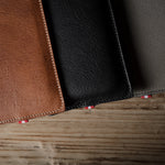 Three leather  iphone cases in brown, black, and gray on a wooden surface.