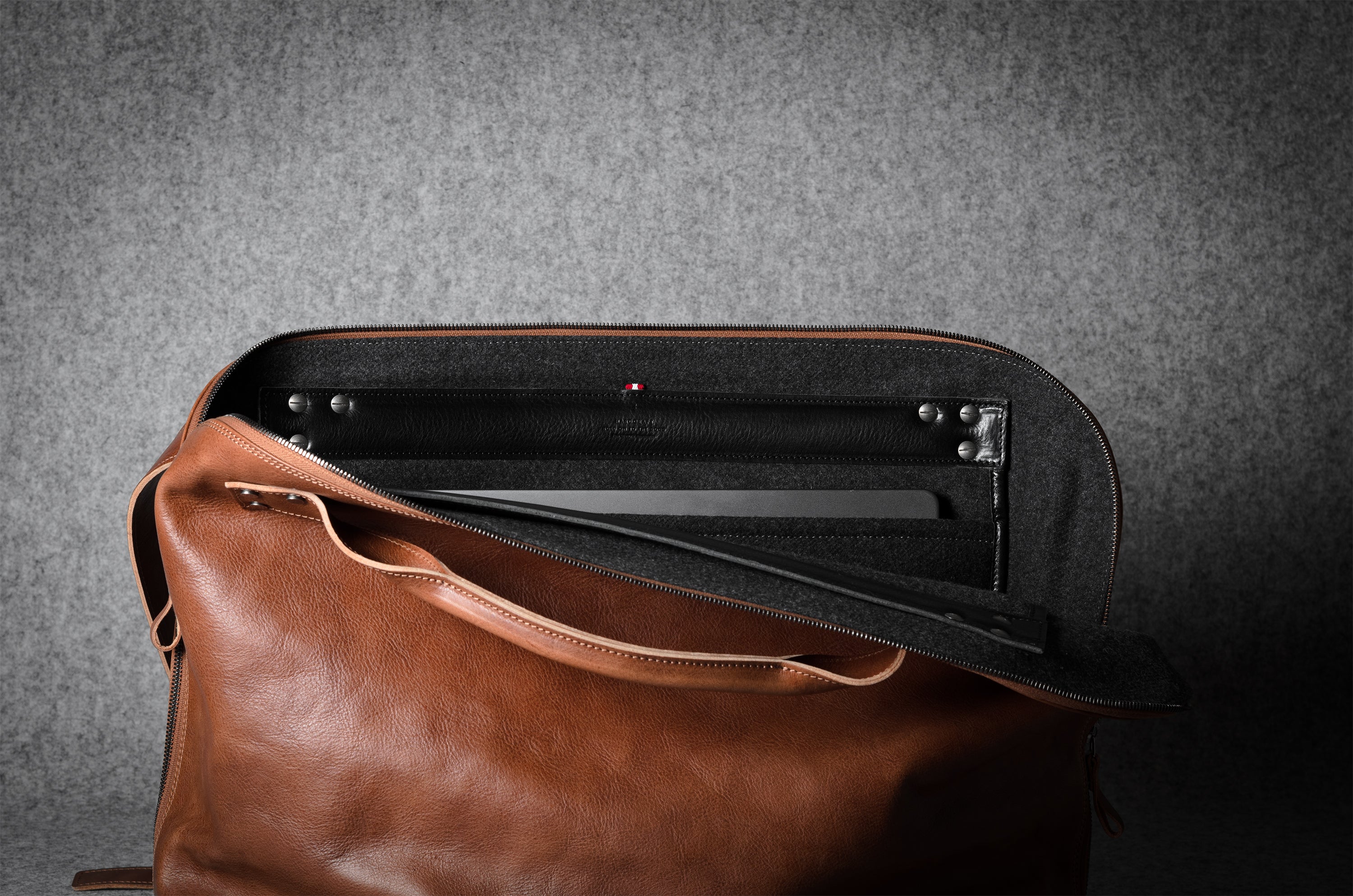 Brown leather laptop bag with a grey interior on a gray background