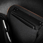 Brown bag showing dark grey interior with a compartment for electronic devices on a dark background