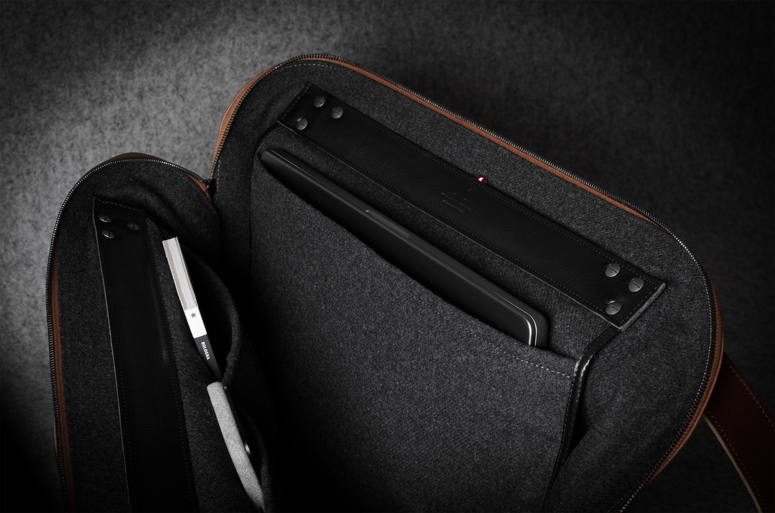 Brown bag showing dark grey interior with a compartment for electronic devices on a dark background