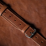 Close-up of a brown leather belt with a buckle on a brown background
