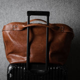 Brown leather duffel bag on a black suitcase against a gray background