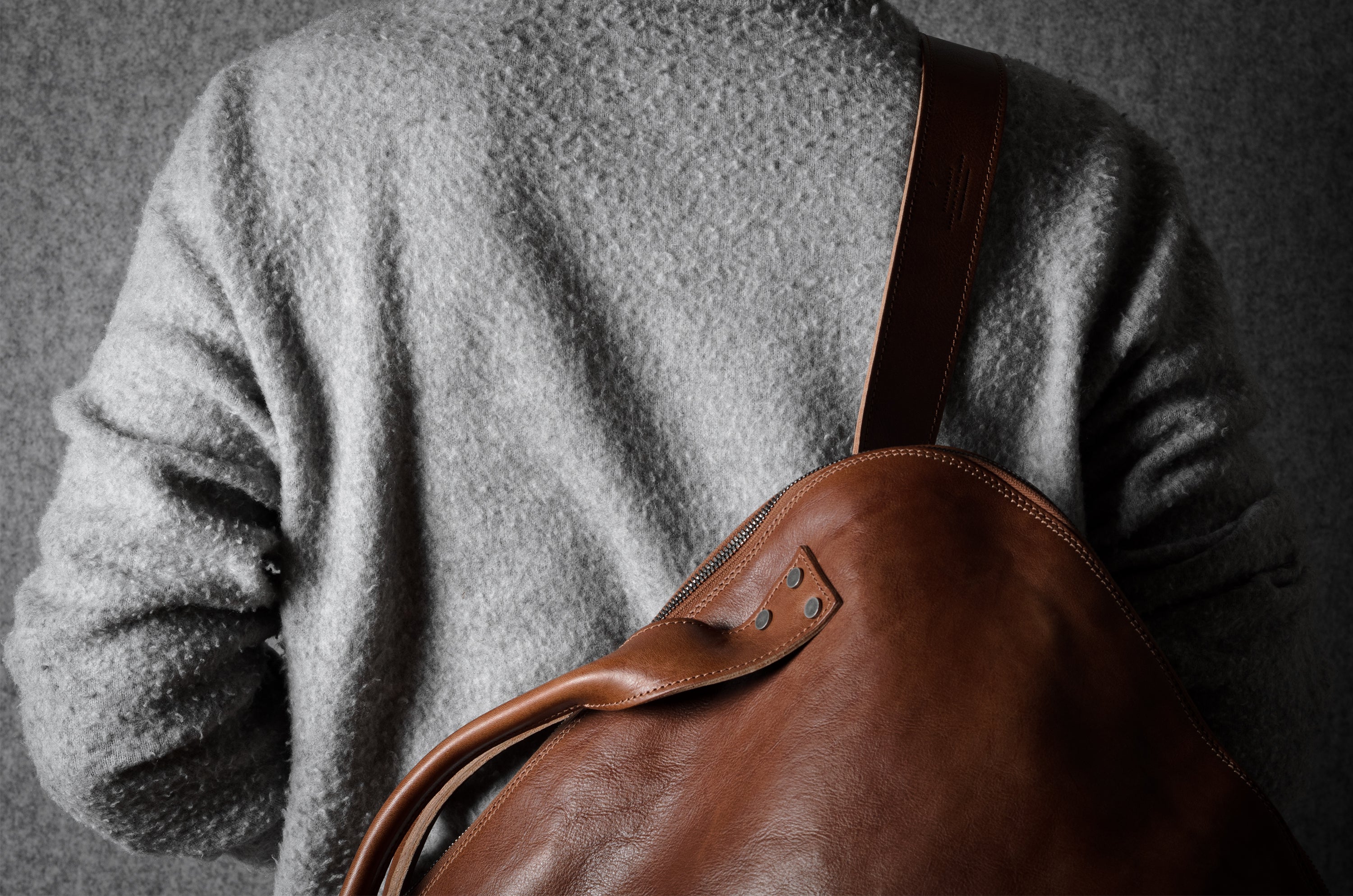 Person wearing a brown leather bag over their shoulder against a dark background