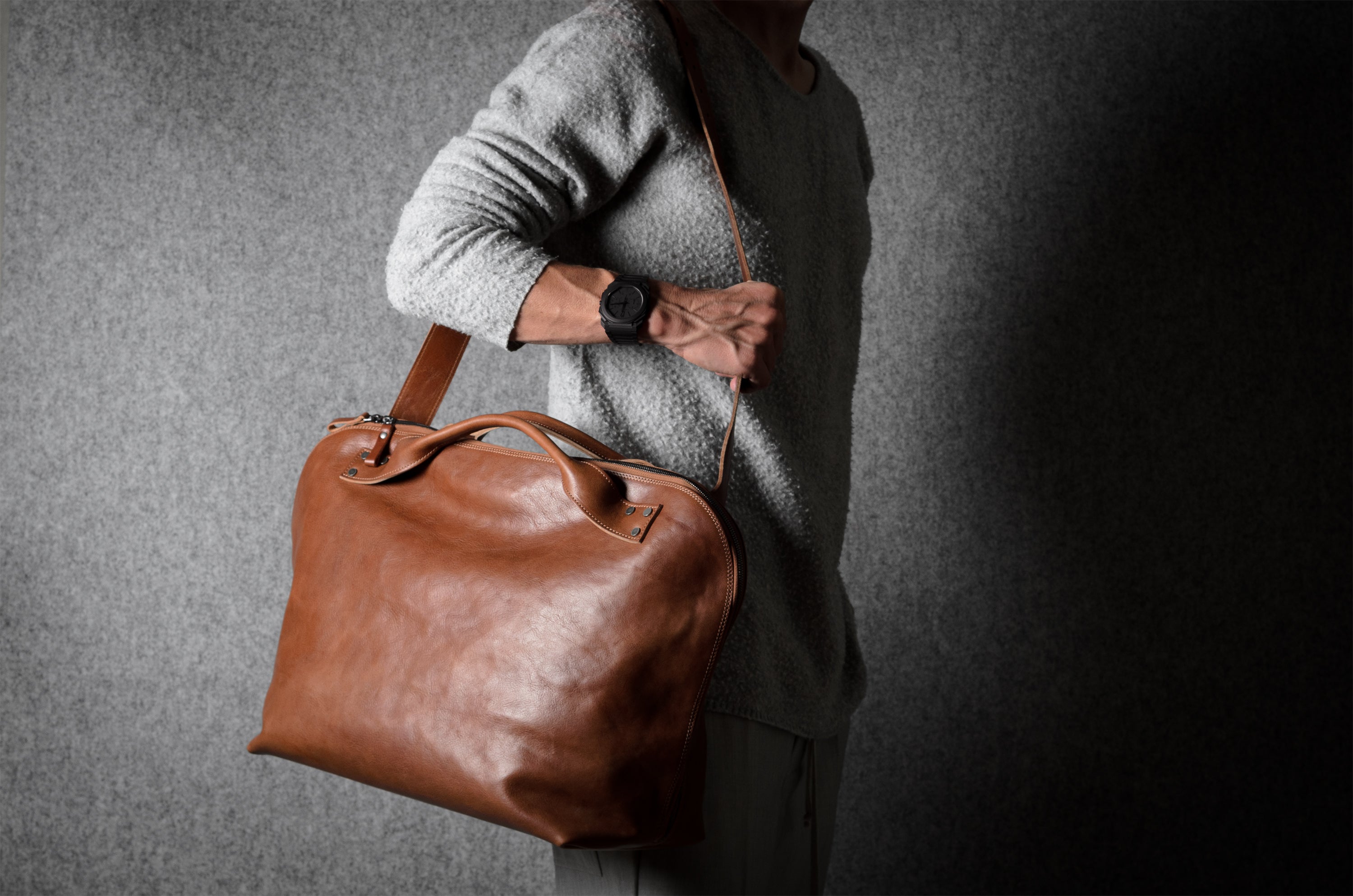 Person holding a brown leather bag against a dark background