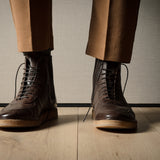 Brown leather boots and pants on a wooden floor with a neutral background