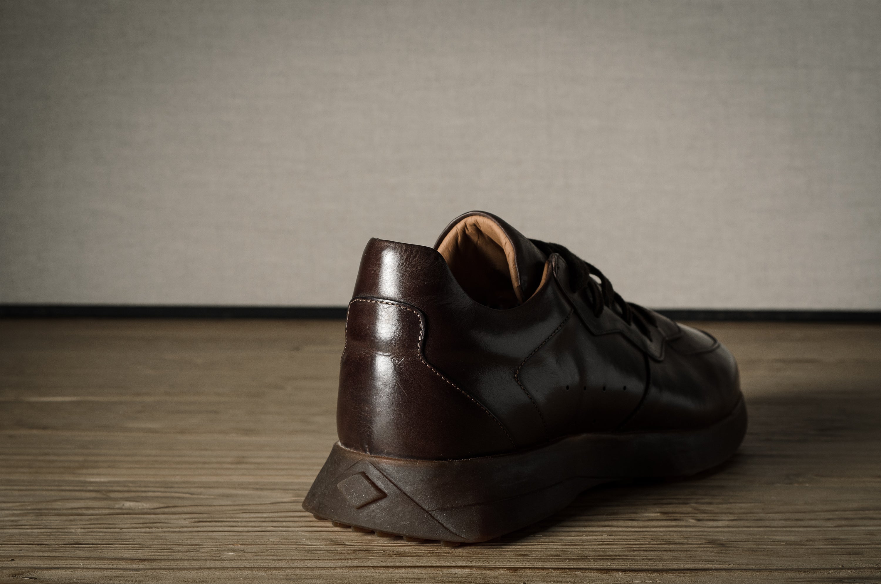 Brown leather sneaker on a wooden floor with a neutral background