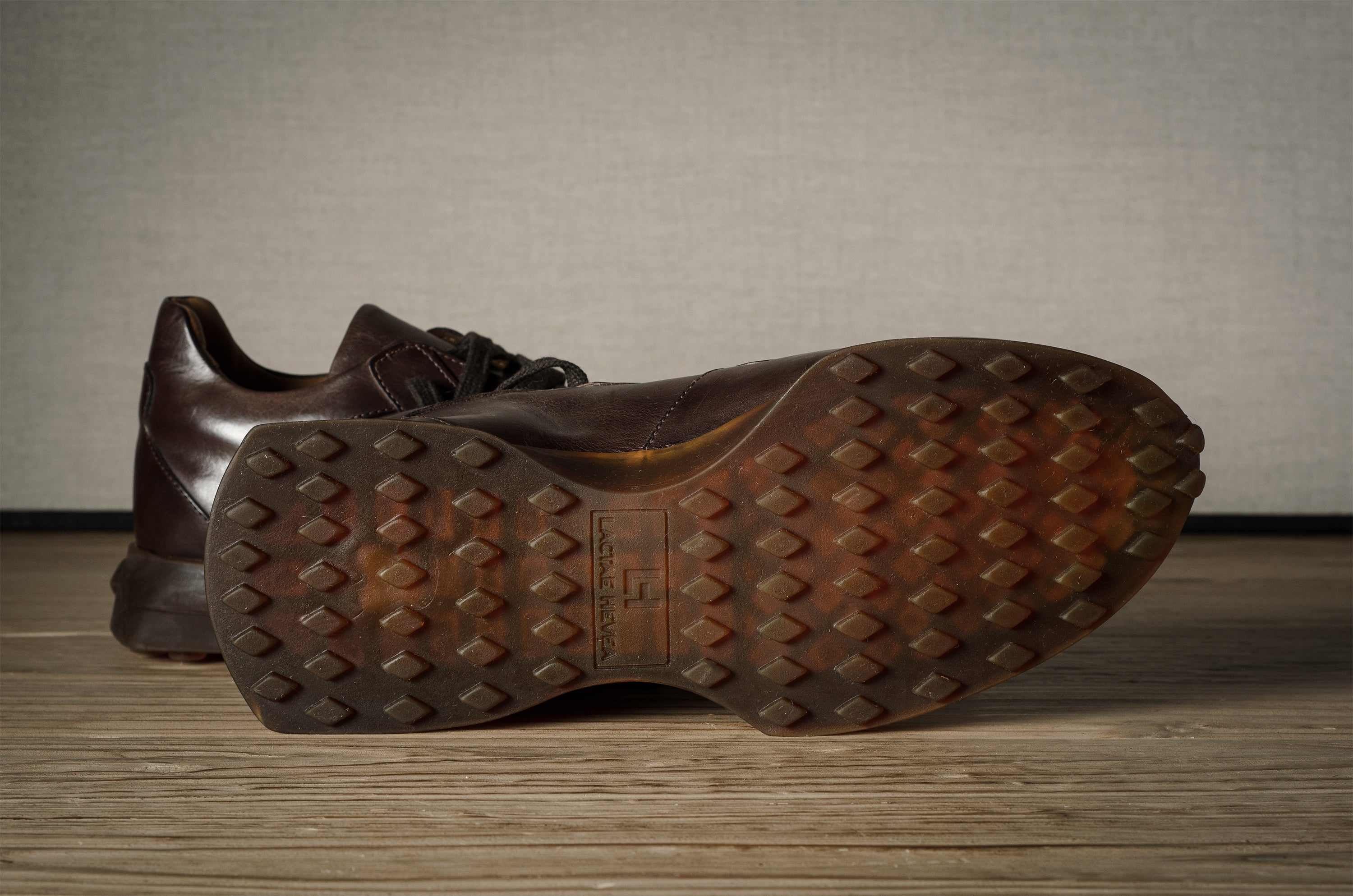 Brown leather sneakers with textured sole on a wooden surface