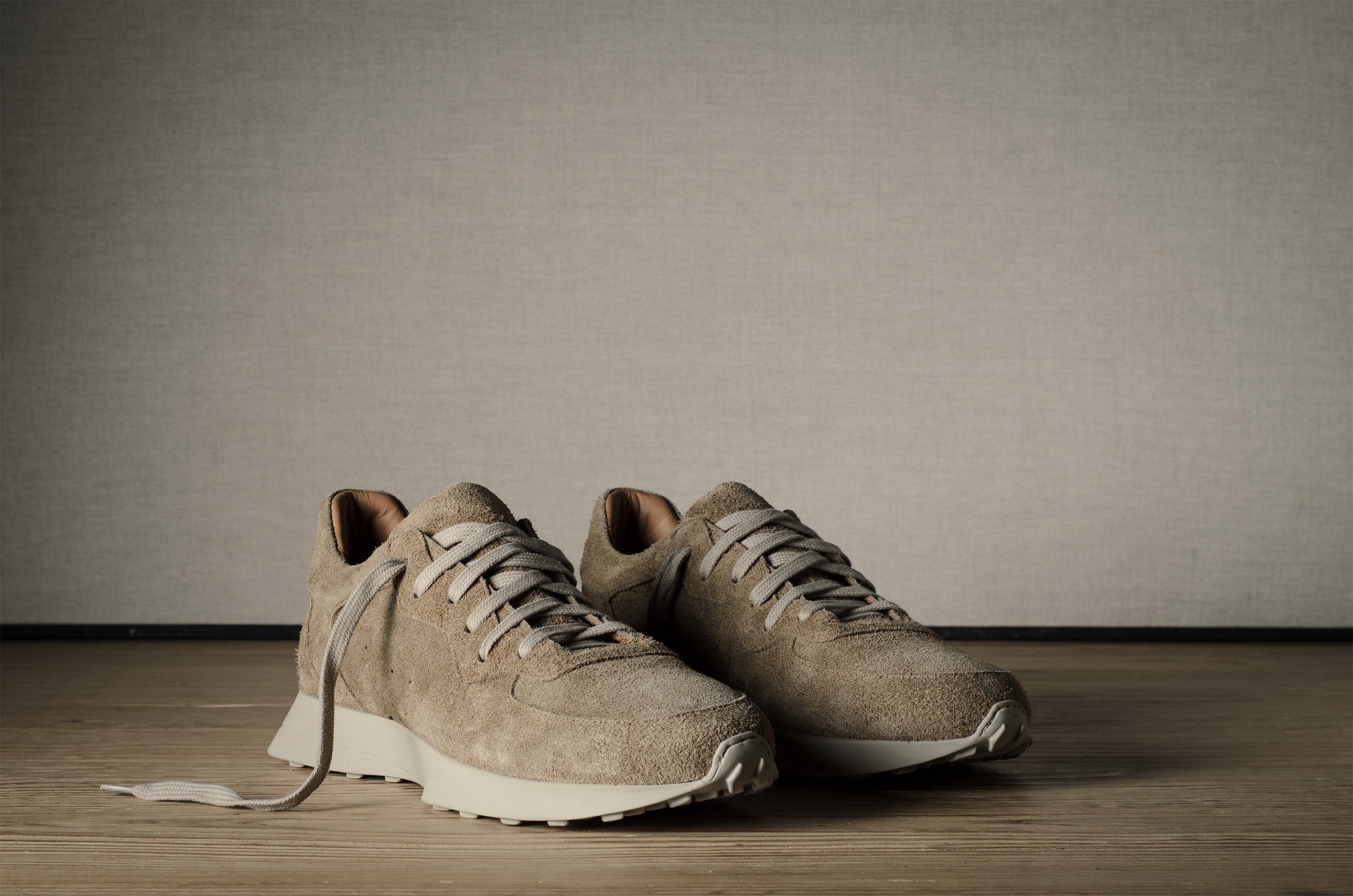 Pair of beige sneakers on a wooden floor with a neutral background